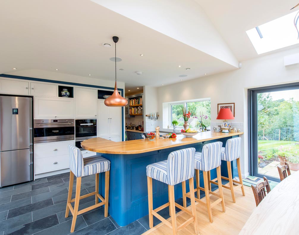 Modern kitchen with blue island, wood countertop, striped bar stools, stainless fridge, and large windows