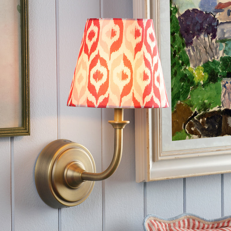 Wall sconce with a colorful lampshade next to a painting and floral arrangement on a light blue wall.