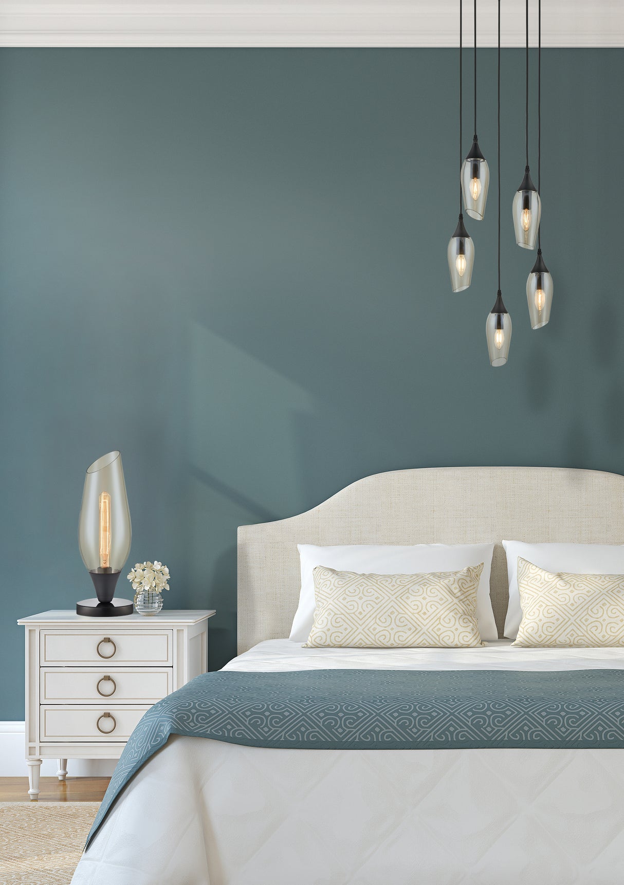 Modern bedroom with beige upholstered bed, decorative pillows, blue patterned blanket, pendant lights, and bedside table with lamp and flowers
