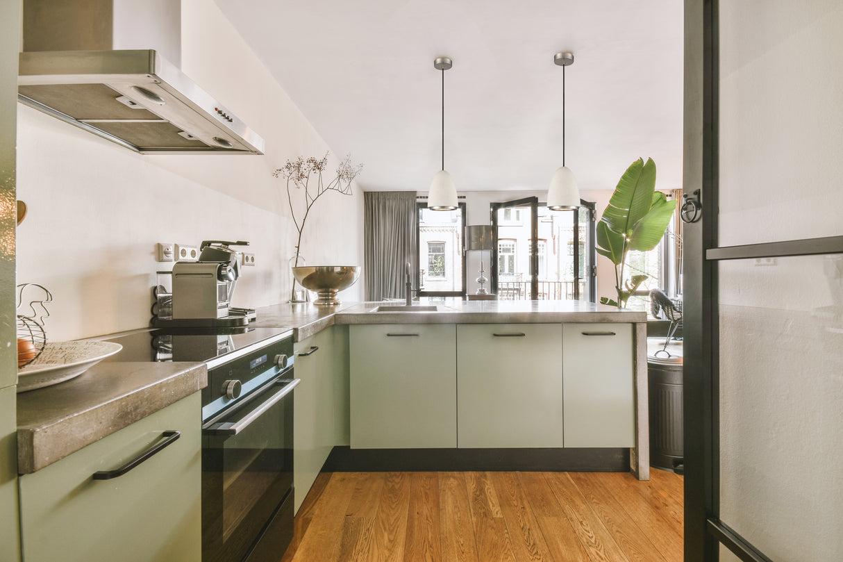 Modern kitchen with green cabinets, concrete countertops, wooden floor, and pendant lights