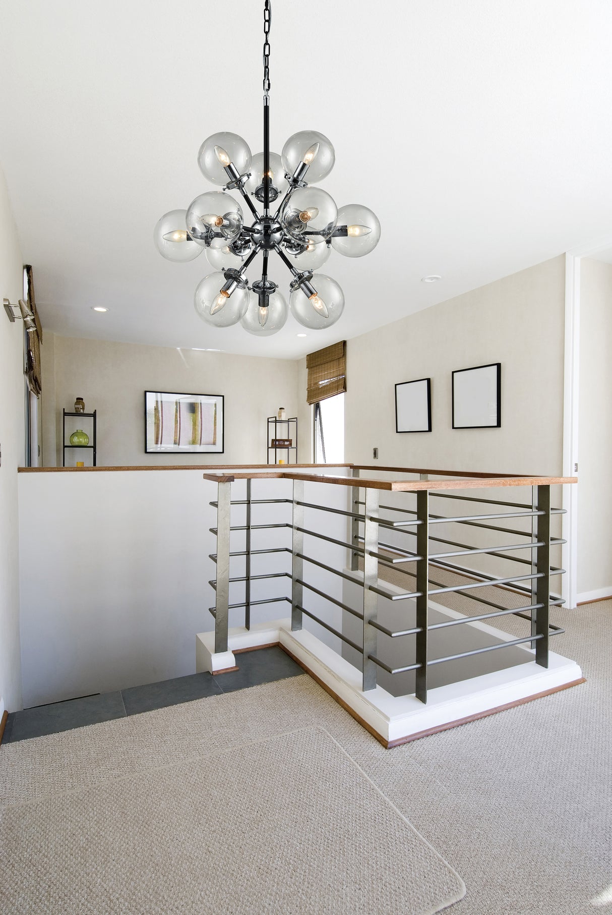 Modern stairwell with metal railing and wood handrails under a black multi-globe glass chandelier