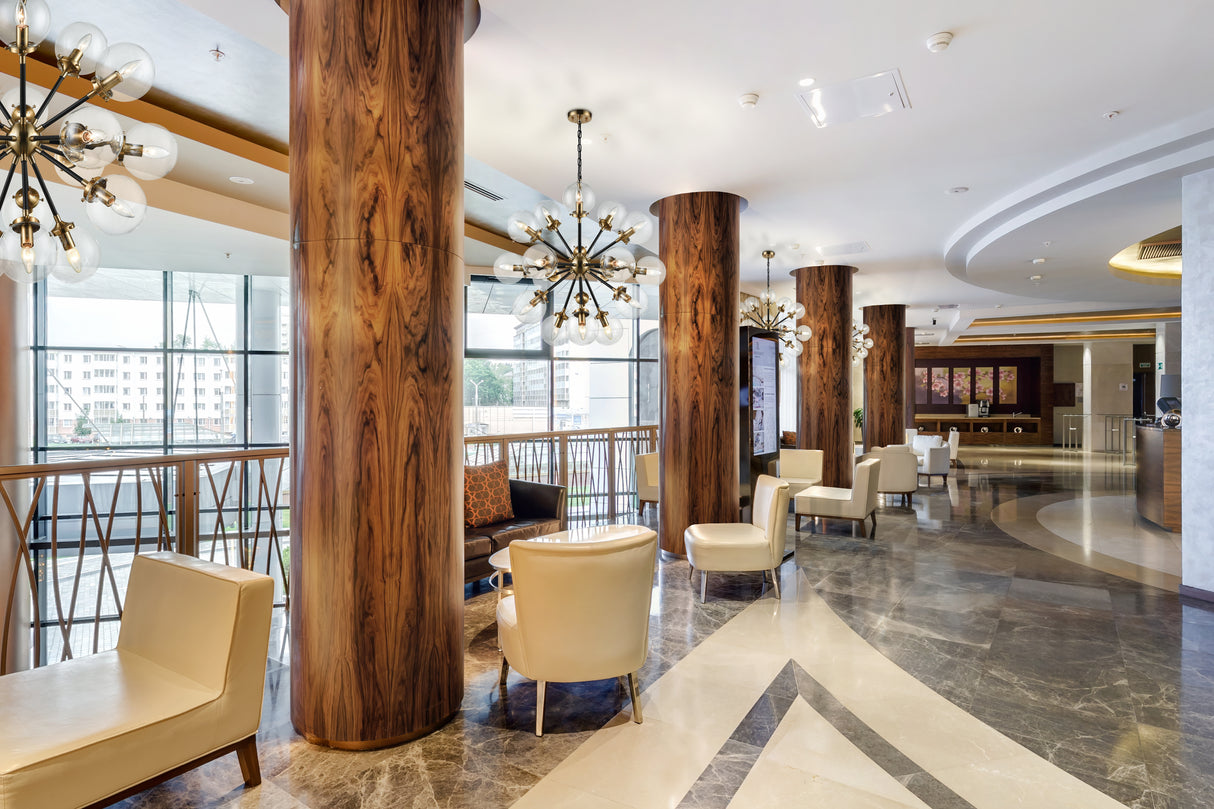 Modern hotel lounge with wood columns, beige leather chairs, chandelier lighting, and marble floor
