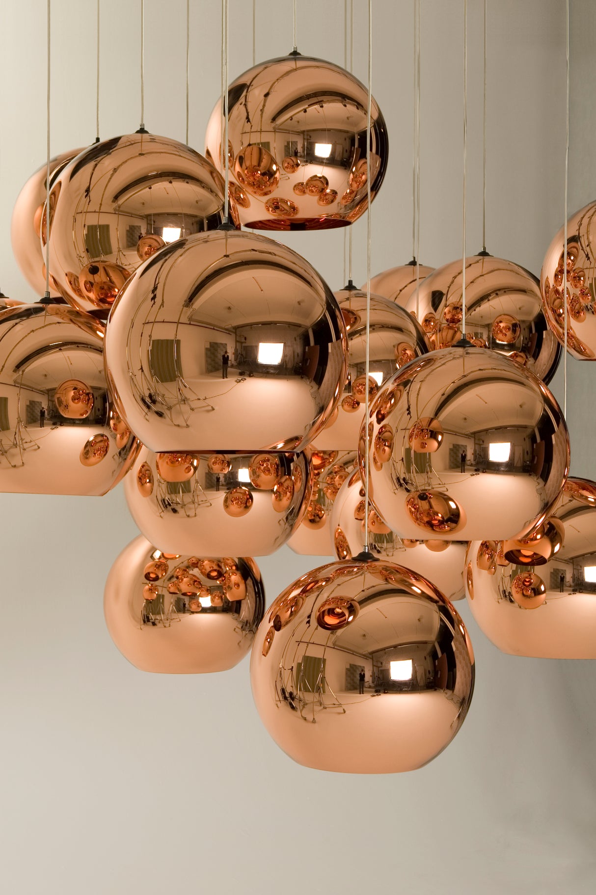 Cluster of shiny copper pendant lights with reflective surfaces hanging in a modern interior.