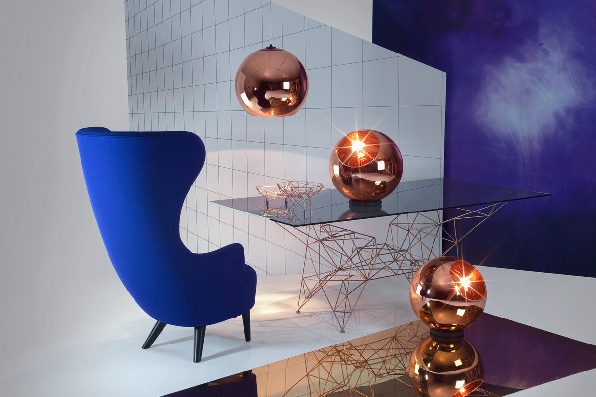 Modern interior with a blue armchair, glass table with copper wire base, and reflective copper globe lights