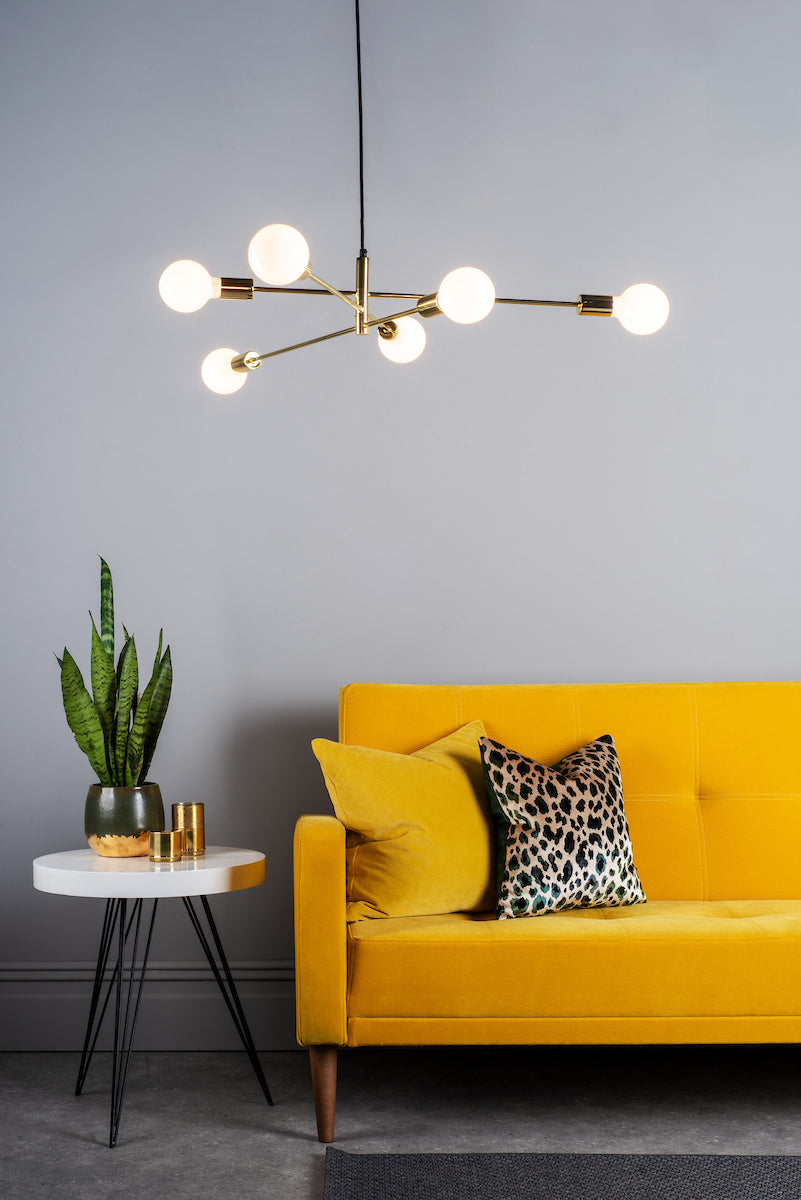 Modern gold pendant chandelier with six glowing bulbs over yellow velvet sofa and side table with plant