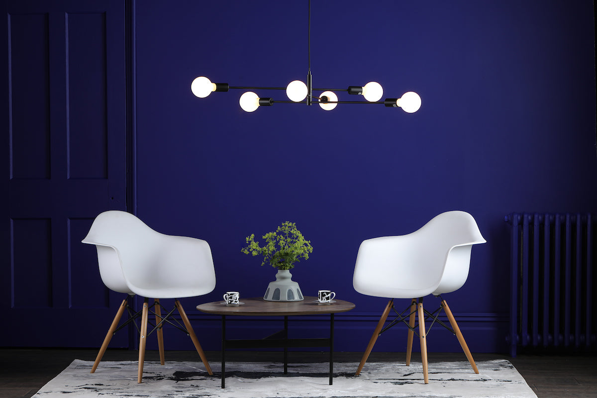 Modern living room with matte black 6-light pendant chandelier, white chairs, wooden table, and blue wall