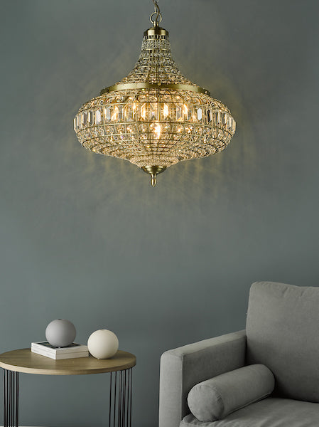 Antique brass 6-light crystal pendant chandelier hanging above modern grey sofa and round wooden side table