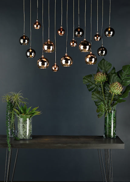 Modern bar pendant lights in black chrome, copper, and bronze above wooden table with green plants in glass vases