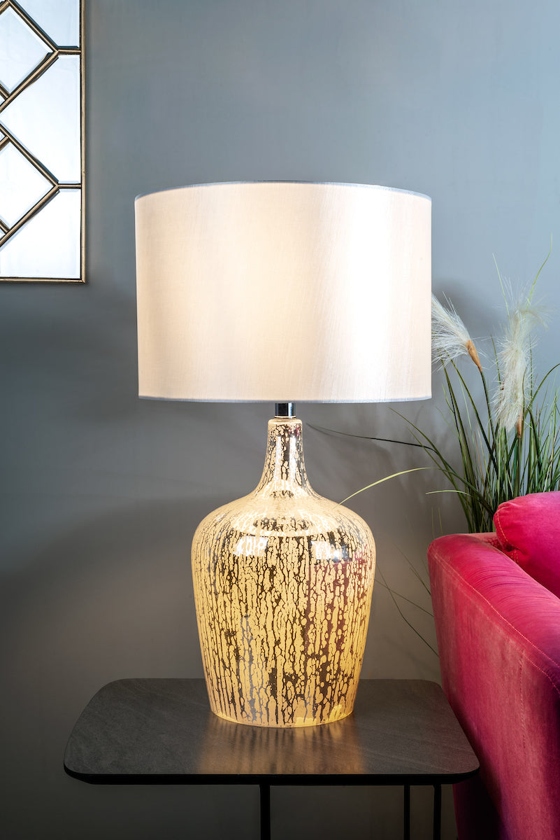 Elegant silver glass table lamp with white shade on black side table near pink sofa and gray wall