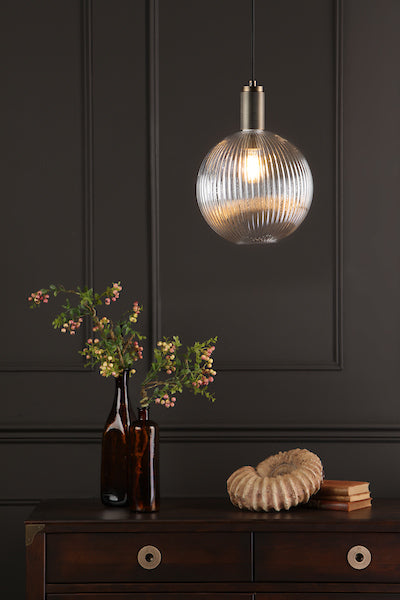 Ribbed round glass pendant light with solid brass fixture above dark wooden cabinet with vases and decorative shell