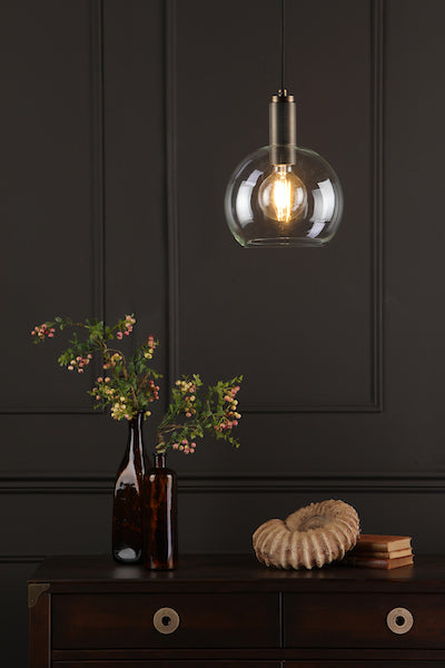 Solid brass pendant light with round glass shade hanging above dark wood dresser featuring brown vases and decorative shell