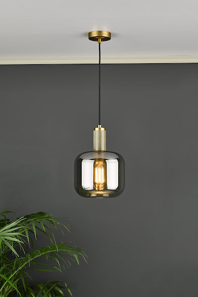 Dar Nikolas solid brass pendant light with smoked glass shade hanging from ceiling against dark gray wall with green plant