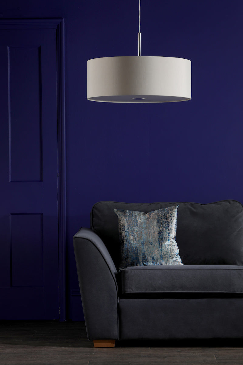 Modern ecru 3-light pendant lamp above dark gray sofa with blue patterned pillow against deep blue wall