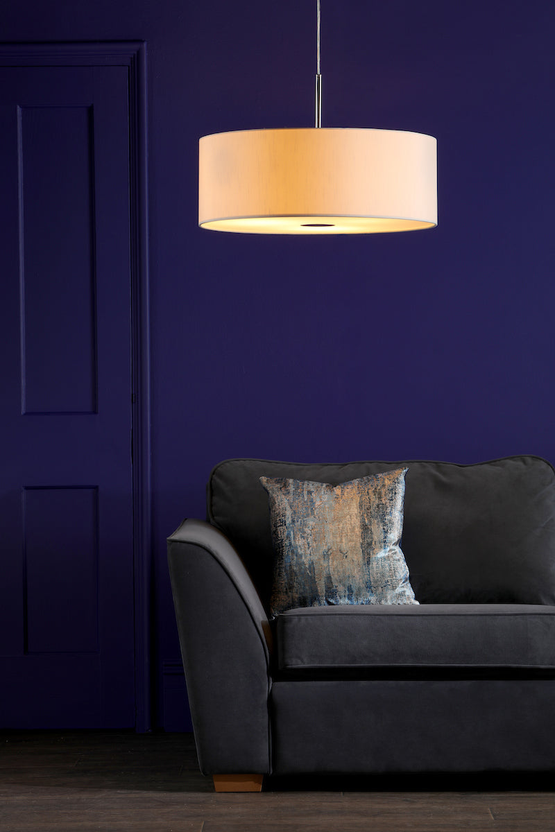 Modern beige pendant light over dark gray sofa with blue patterned pillow against deep purple wall