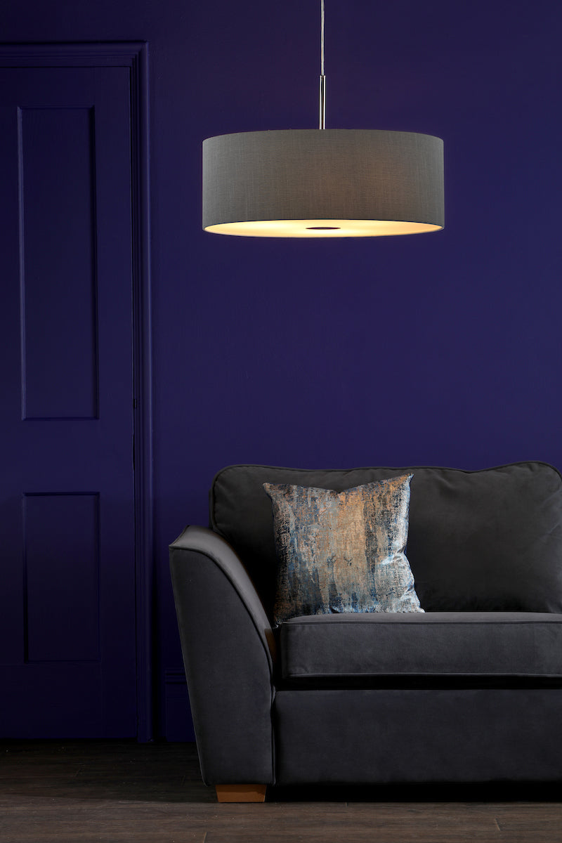 Slate grey drum pendant light above dark grey sofa with textured pillow against purple wall