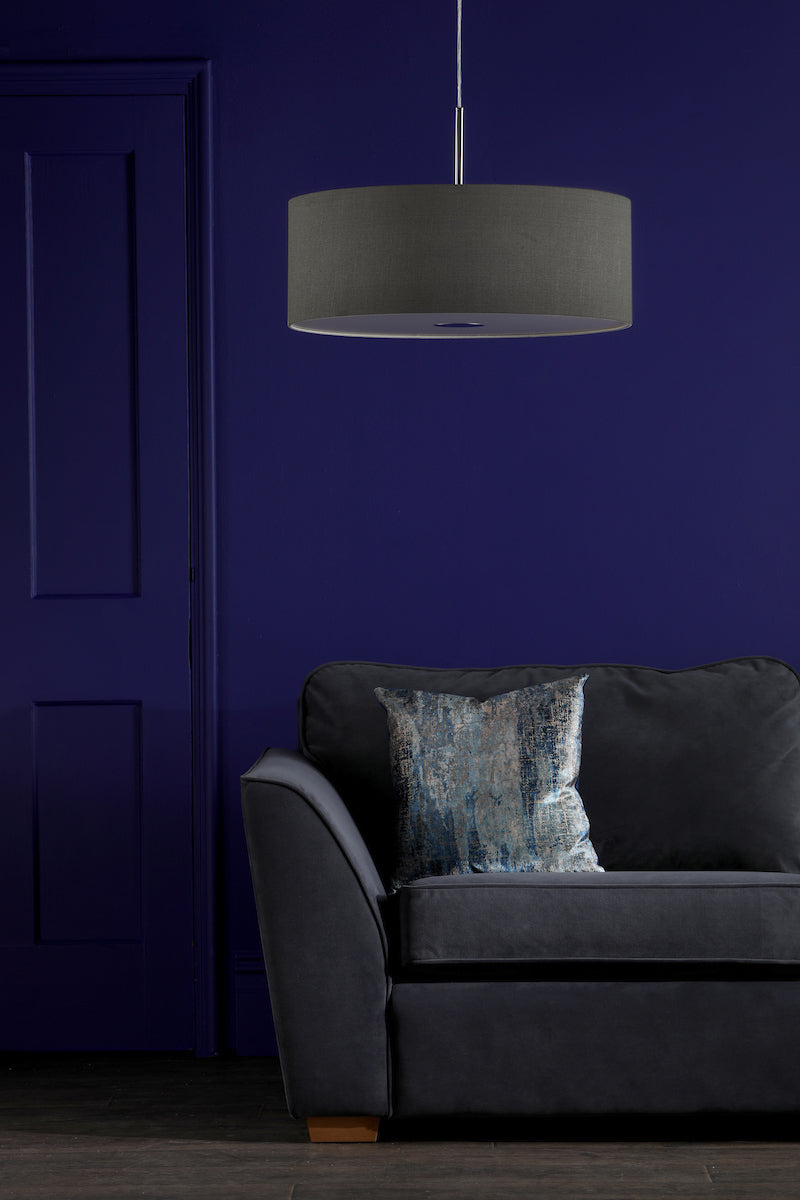 Modern slate grey pendant light above dark grey sofa with textured blue pillow against blue wall