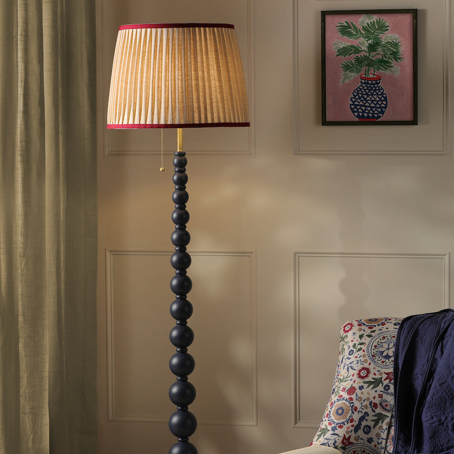 Decorative floor lamp with pleated shade in a room with a floral armchair and framed artwork.
