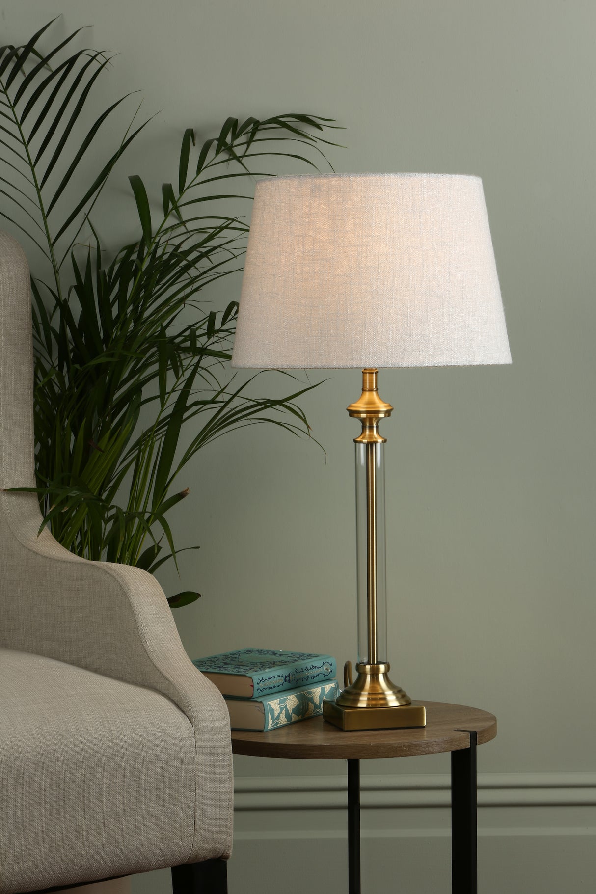 Elegant brass table lamp with white fabric shade on wooden side table beside beige armchair and green plant