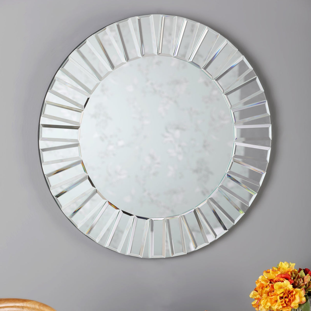 Round decorative wall mirror with faceted beveled glass frame on gray wall