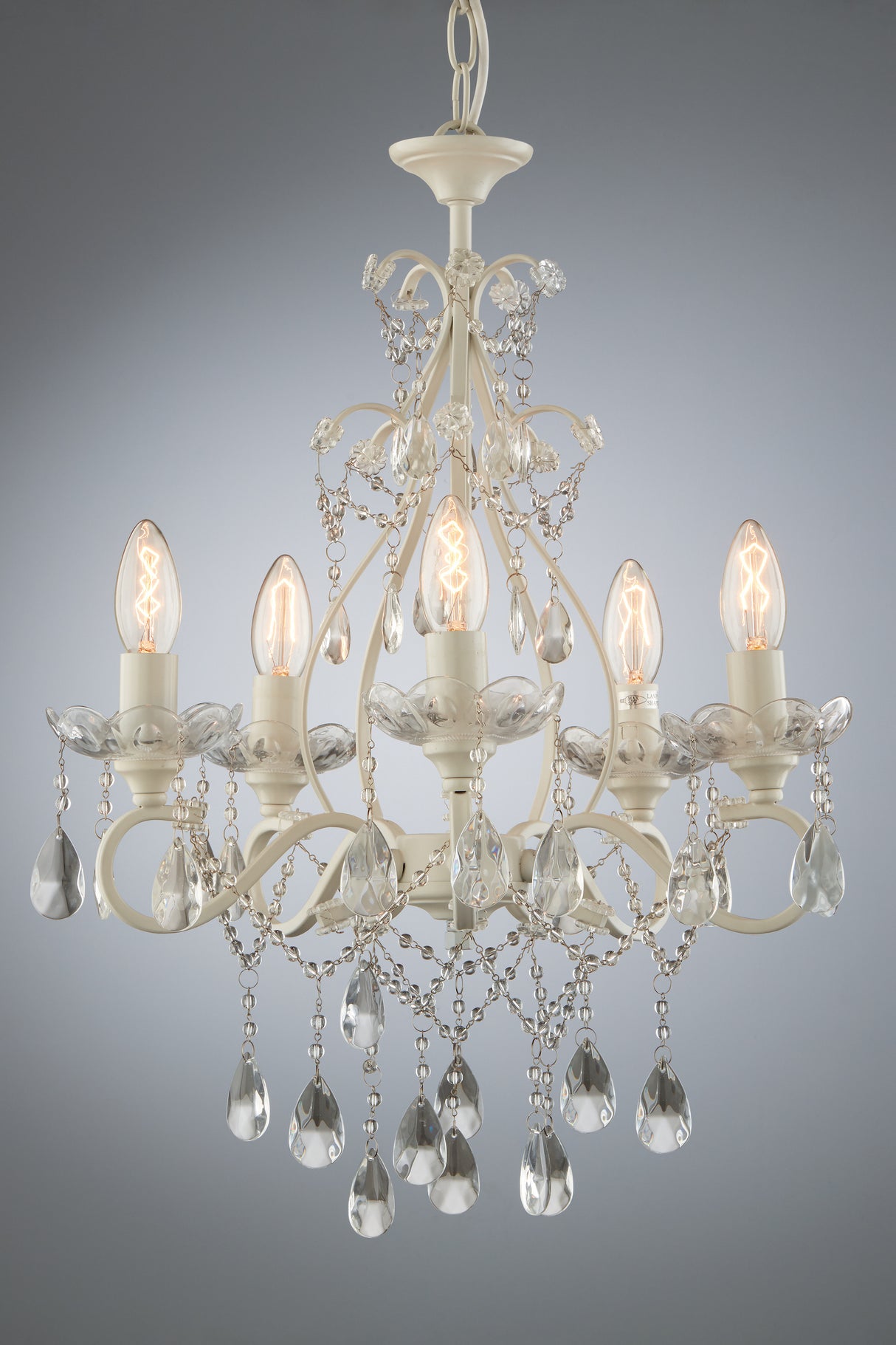 Elegant white chandelier with five glowing bulbs and hanging crystal droplets