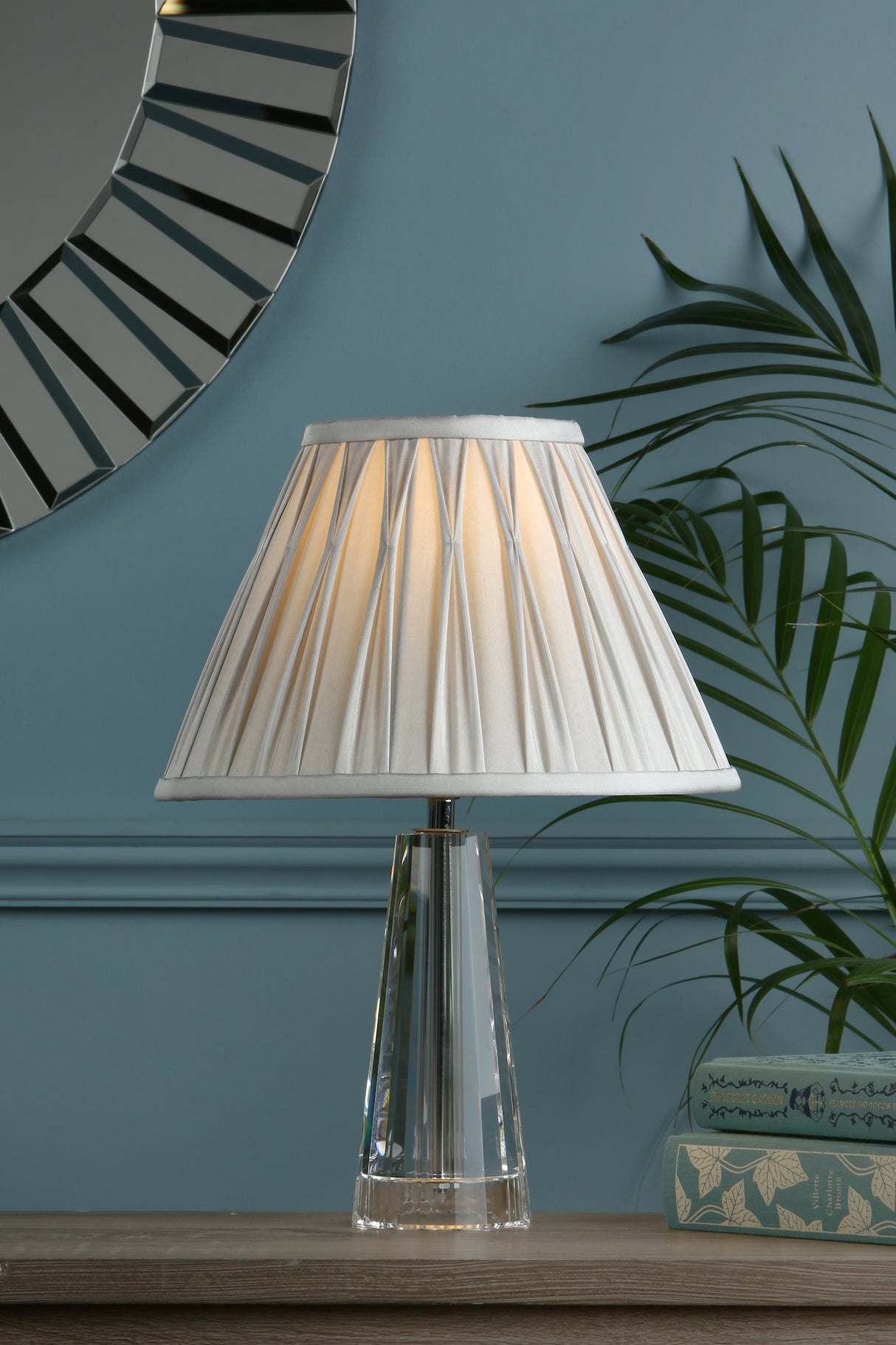 Elegant table lamp with pleated white shade and clear glass base on wooden surface
