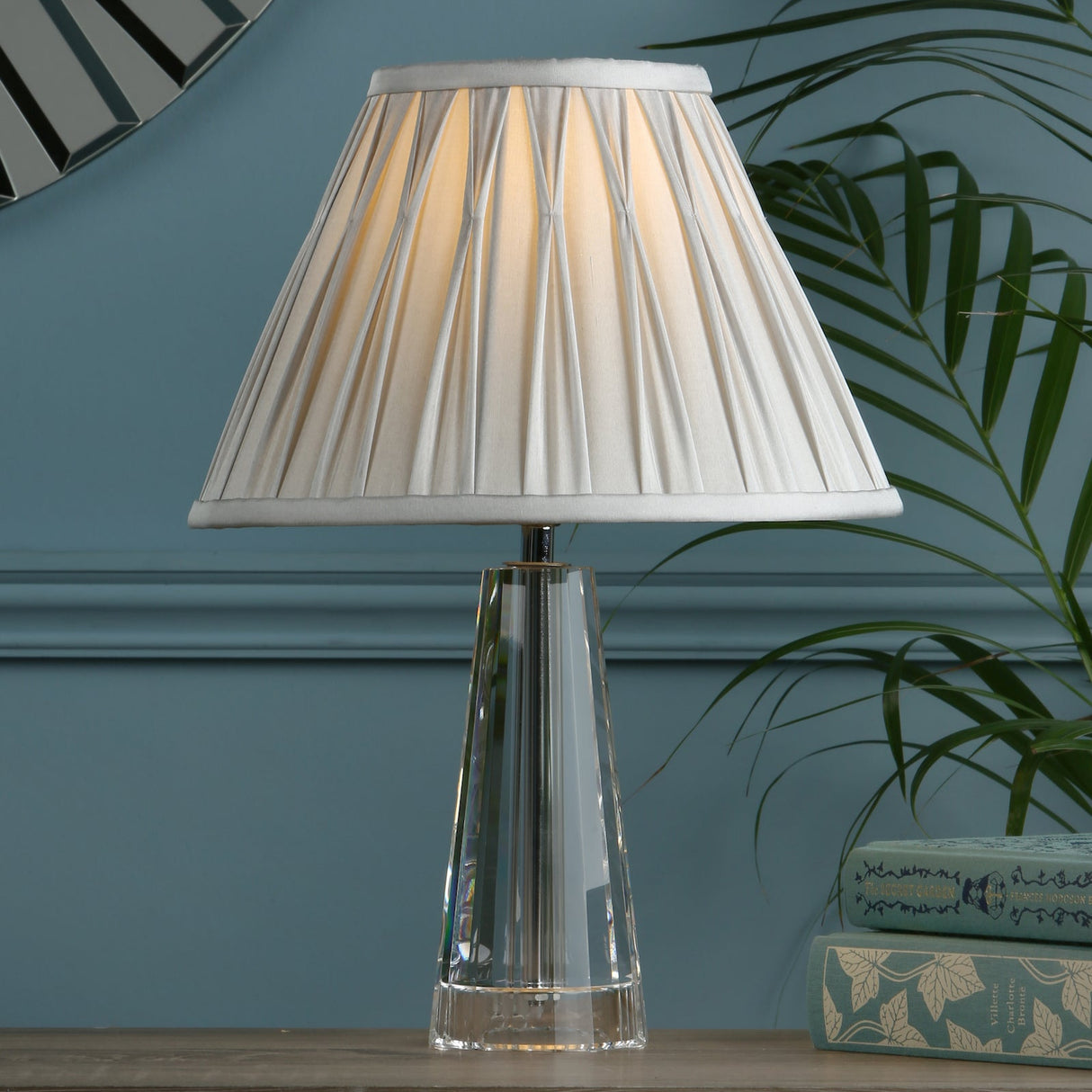 Modern table lamp with pleated white shade and transparent crystal base on wooden table