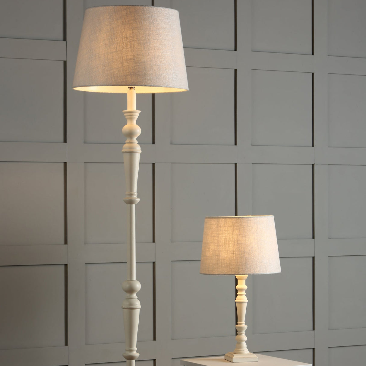 Tall floor lamp and small table lamp with beige fabric shades against gray panel wall