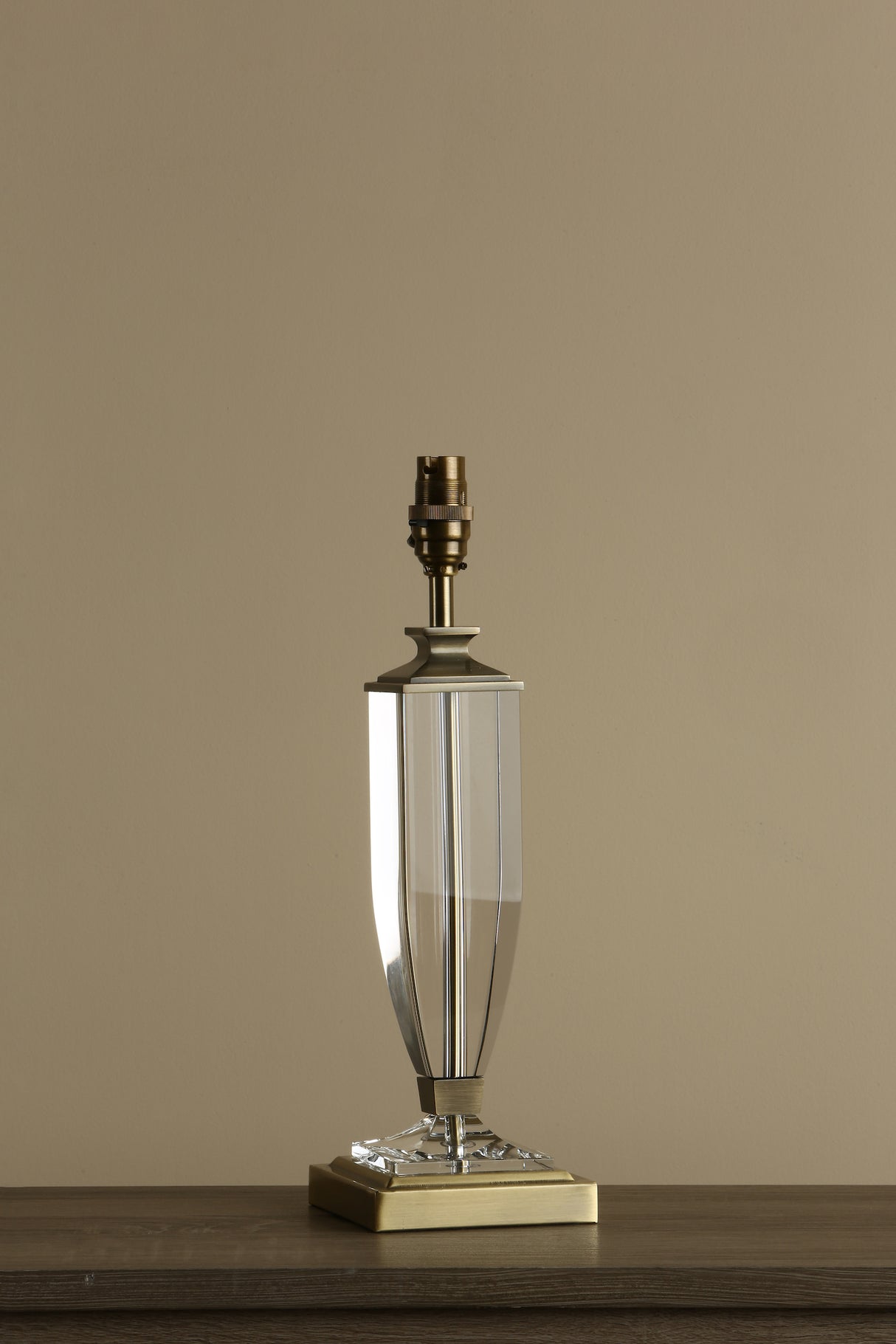 Modern clear crystal table lamp base with brass accents on wooden surface