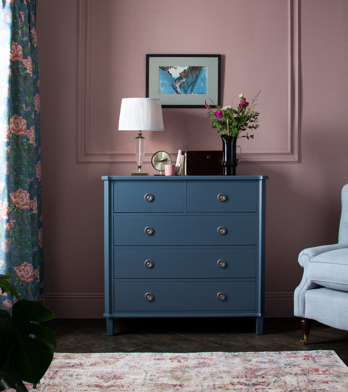 Blue chest of drawers with lamp, clock, flowers on pink wall in elegant living room