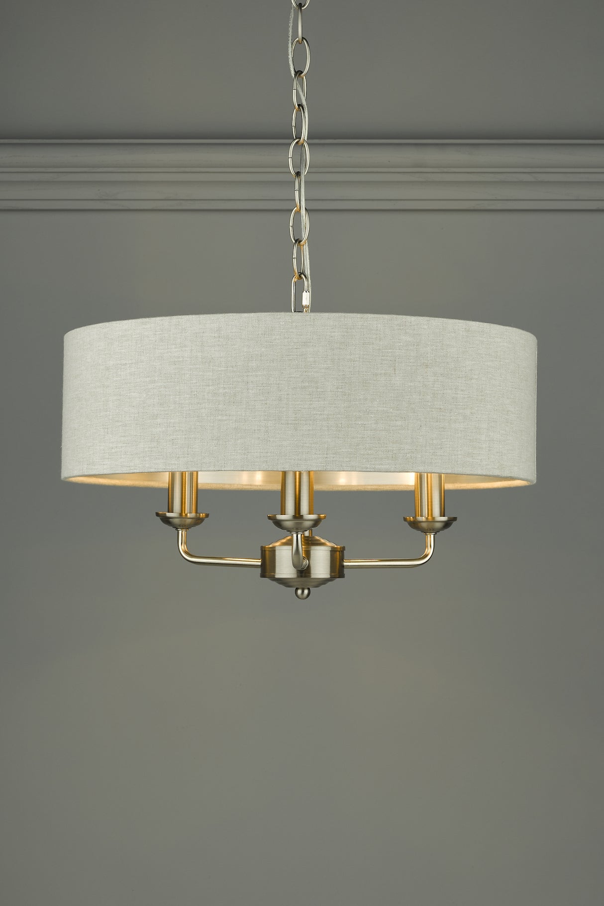 Modern chandelier with beige fabric drum shade and brushed brass metal frame hanging from chain
