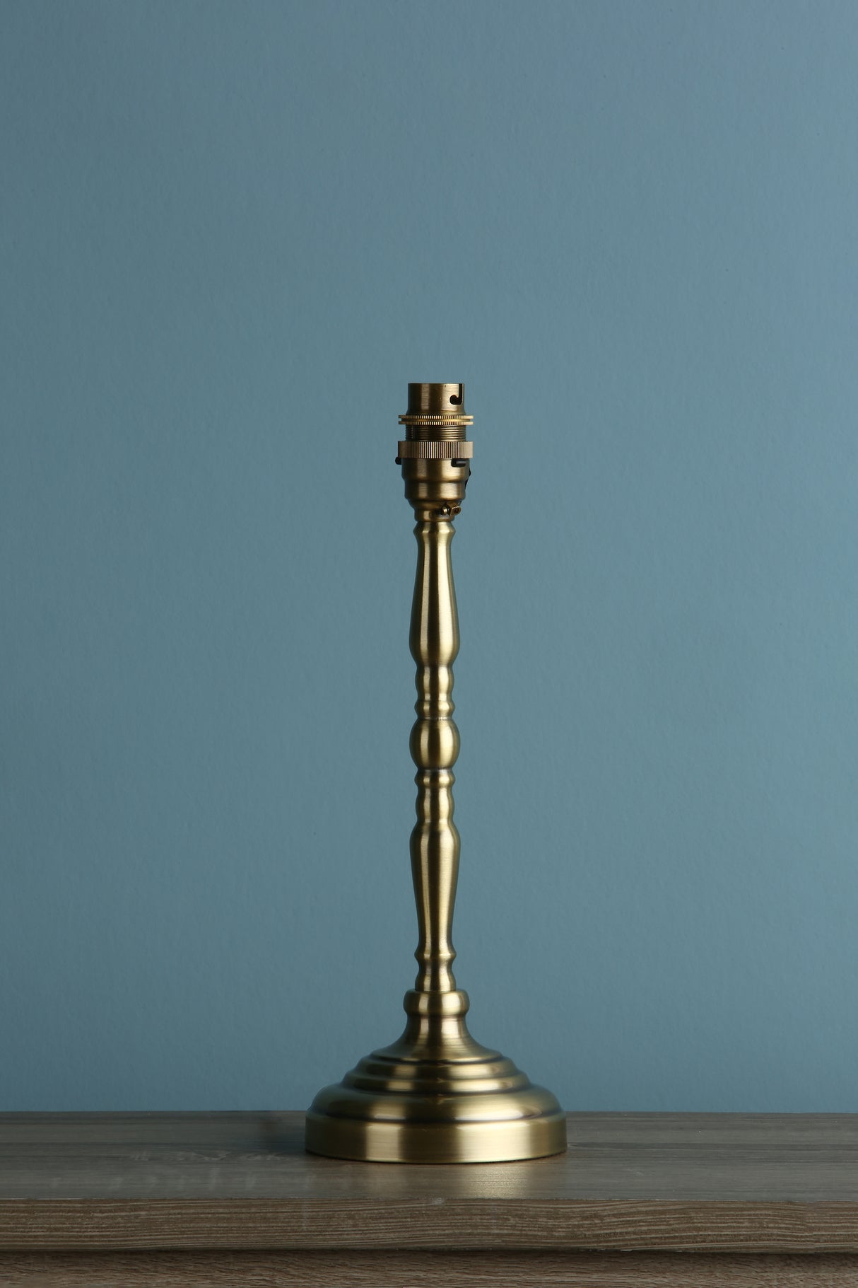 Brushed brass table lamp base with vintage design on wooden surface against blue wall