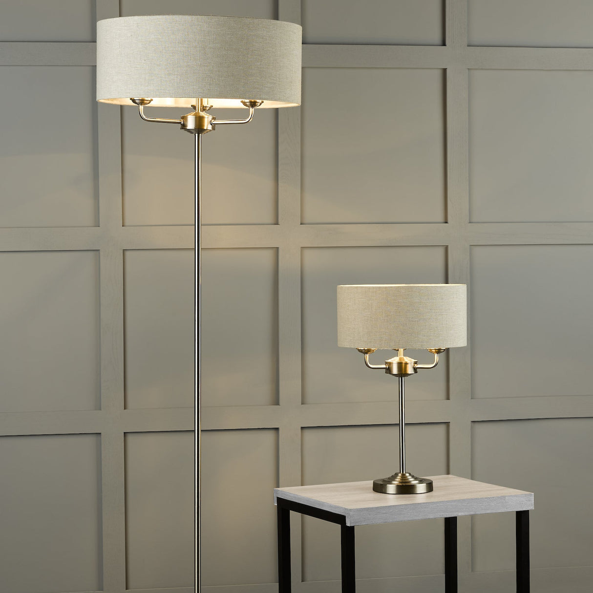 Beige fabric shade floor lamp and matching table lamp on light wooden side table against gray paneled wall