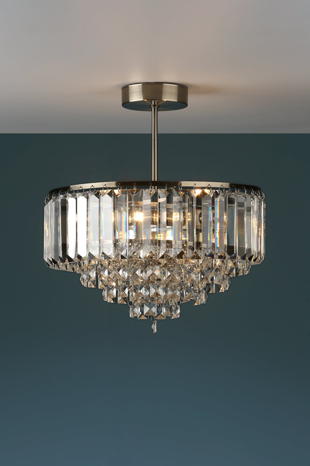 Elegant crystal chandelier with brass frame mounted on ceiling against dark teal wall
