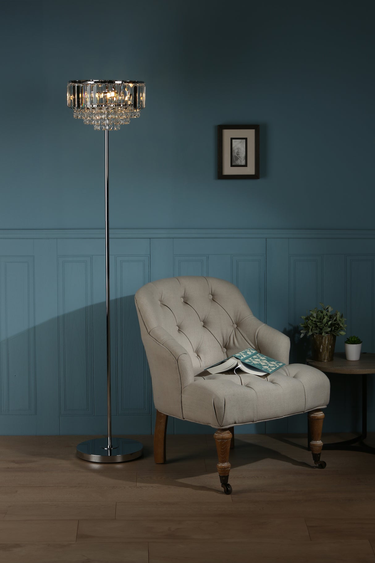 Beige tufted armchair with open book, crystal floor lamp, small table with plants in blue walled room