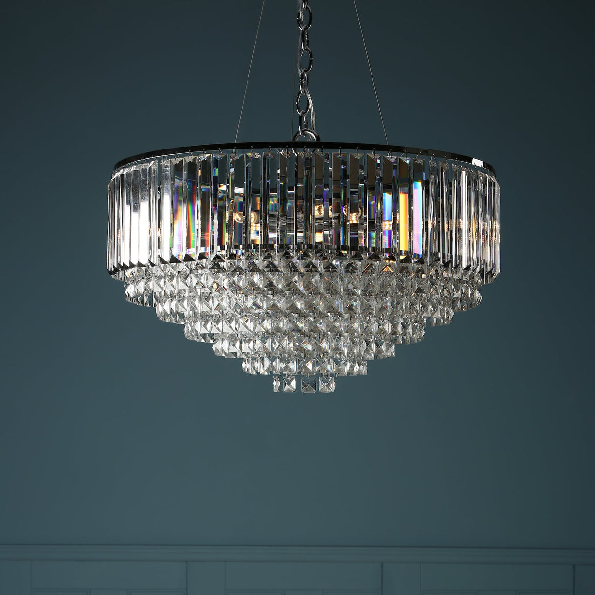 Elegant crystal chandelier with layered prisms and hanging chain against dark background