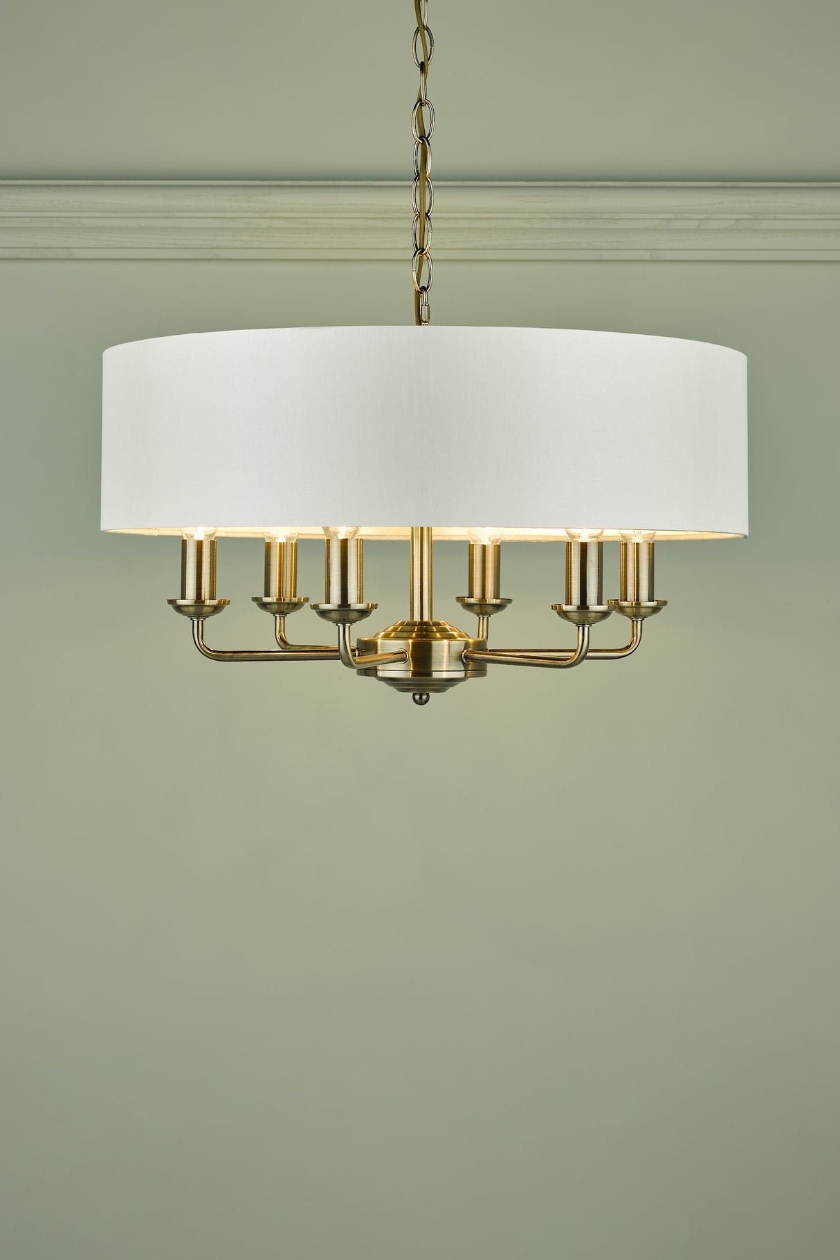 Modern brass chandelier with white drum shade and six candle-style lights against light grey wall