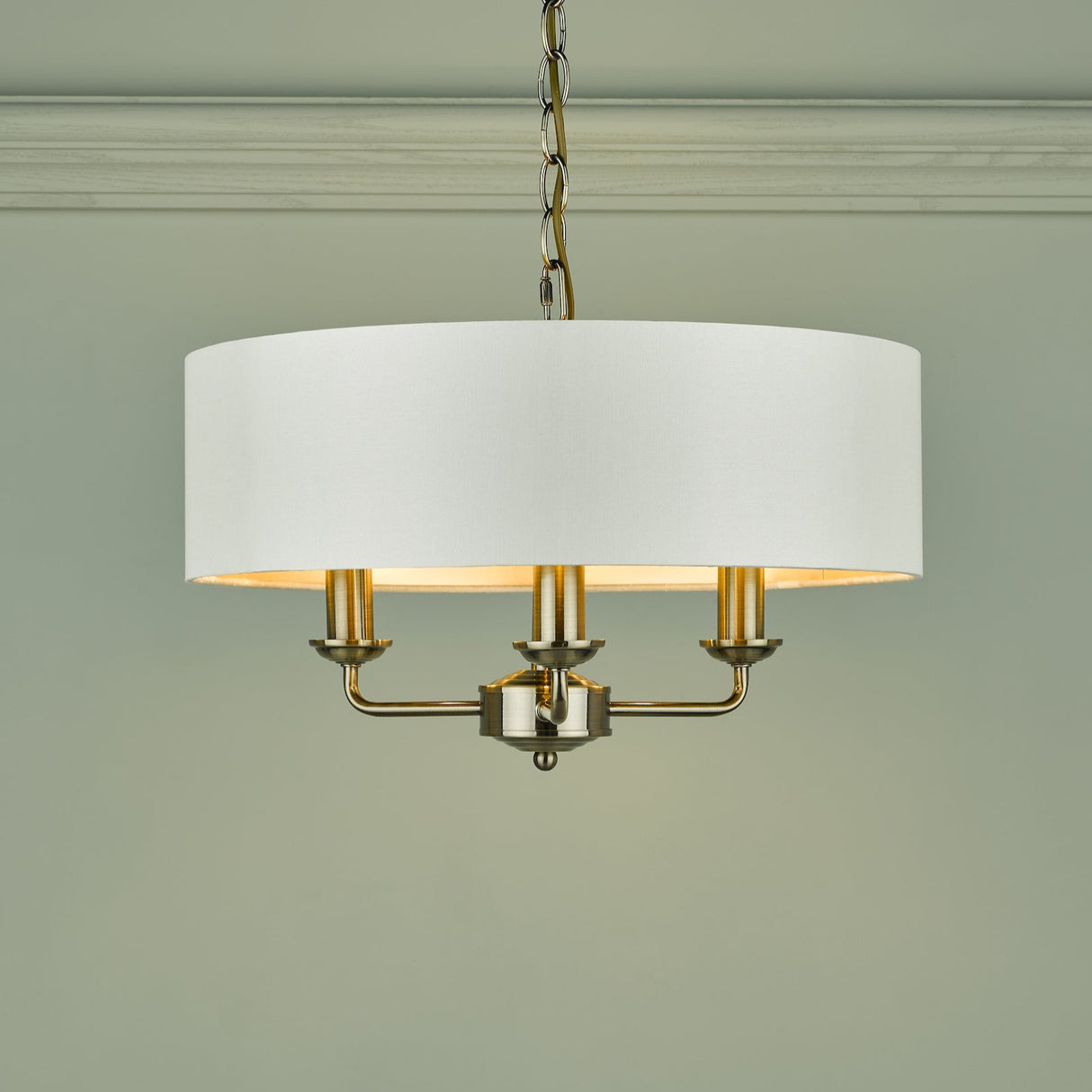 Modern chandelier with white drum shade and brushed brass candle-style lights hanging from chain