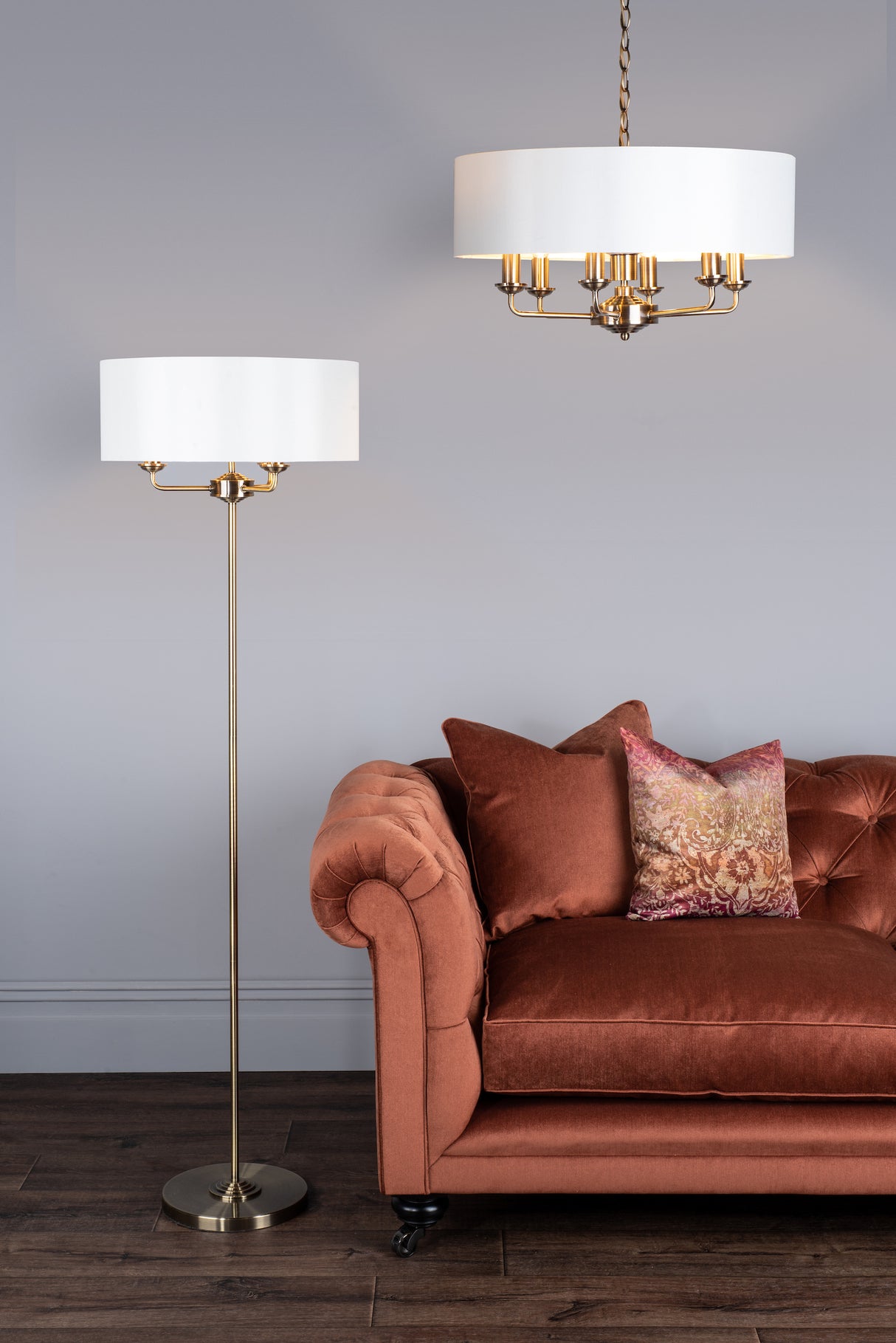 Brown velvet tufted sofa with patterned pillow next to brass floor lamp and white drum pendant light