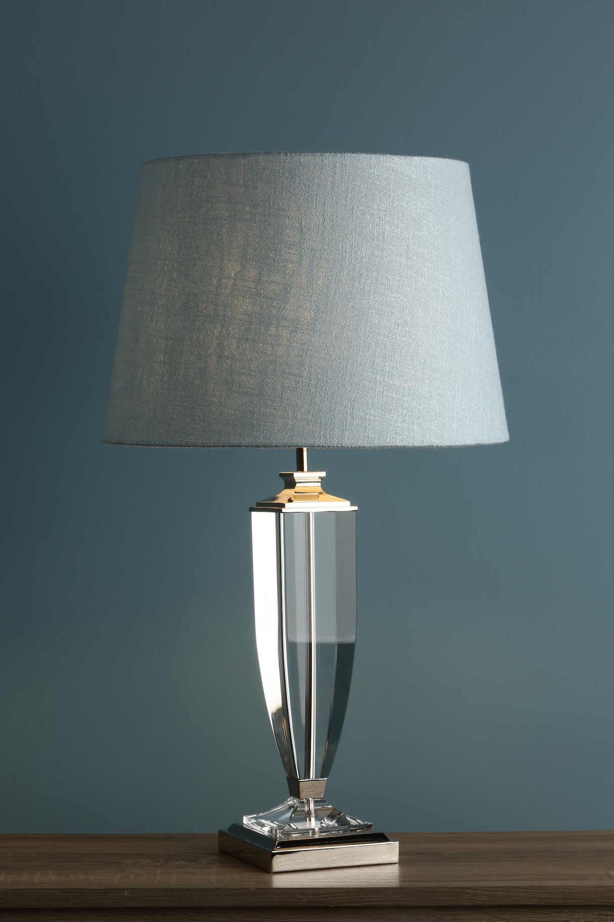 Modern table lamp with clear glass base and light gray fabric shade on wooden surface
