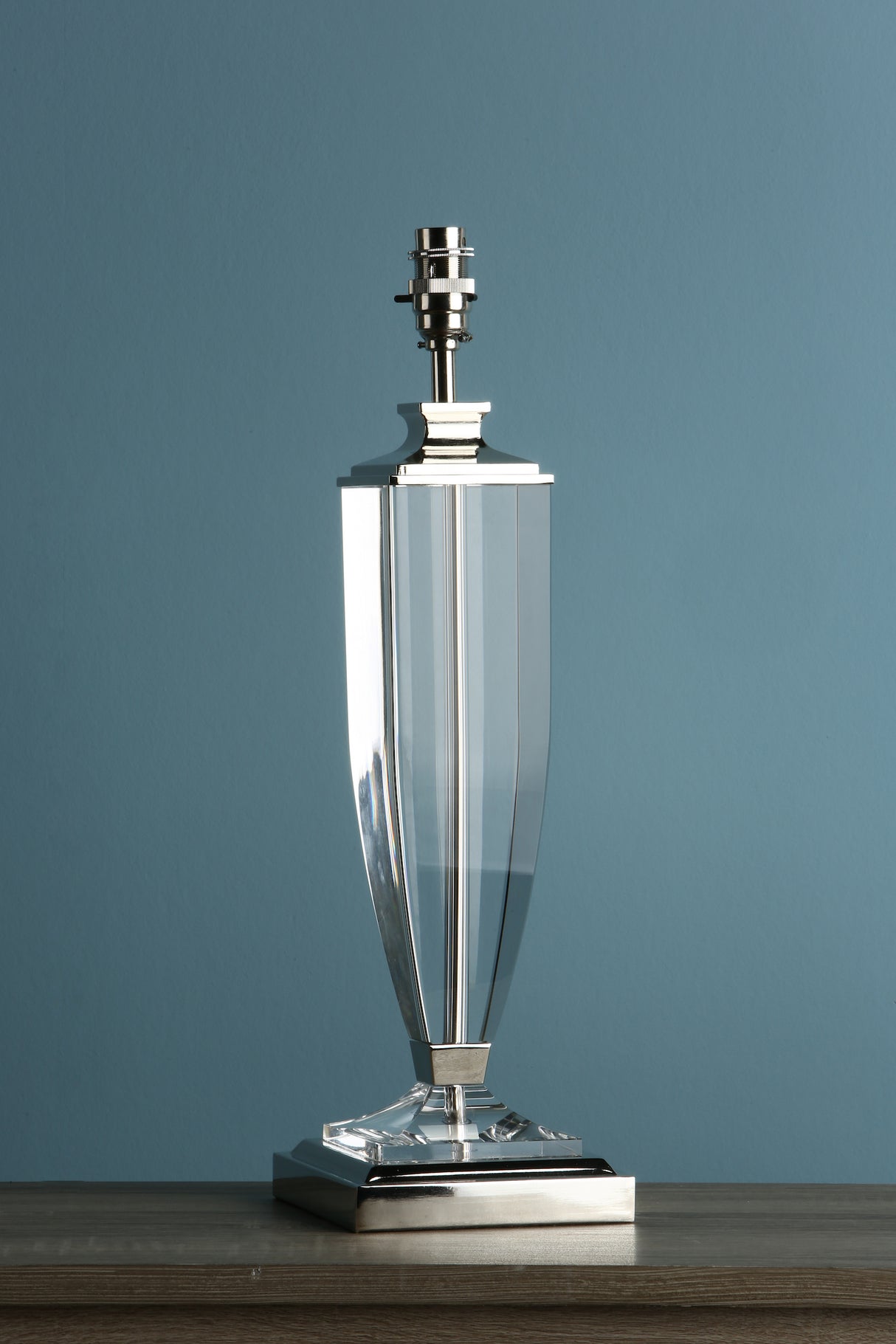 Modern clear glass and metallic table lamp base on wooden surface with blue background