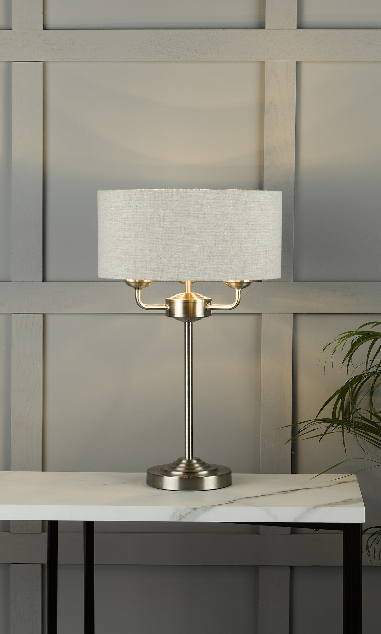 Modern table lamp with brushed metal base and light beige fabric shade on white marble table