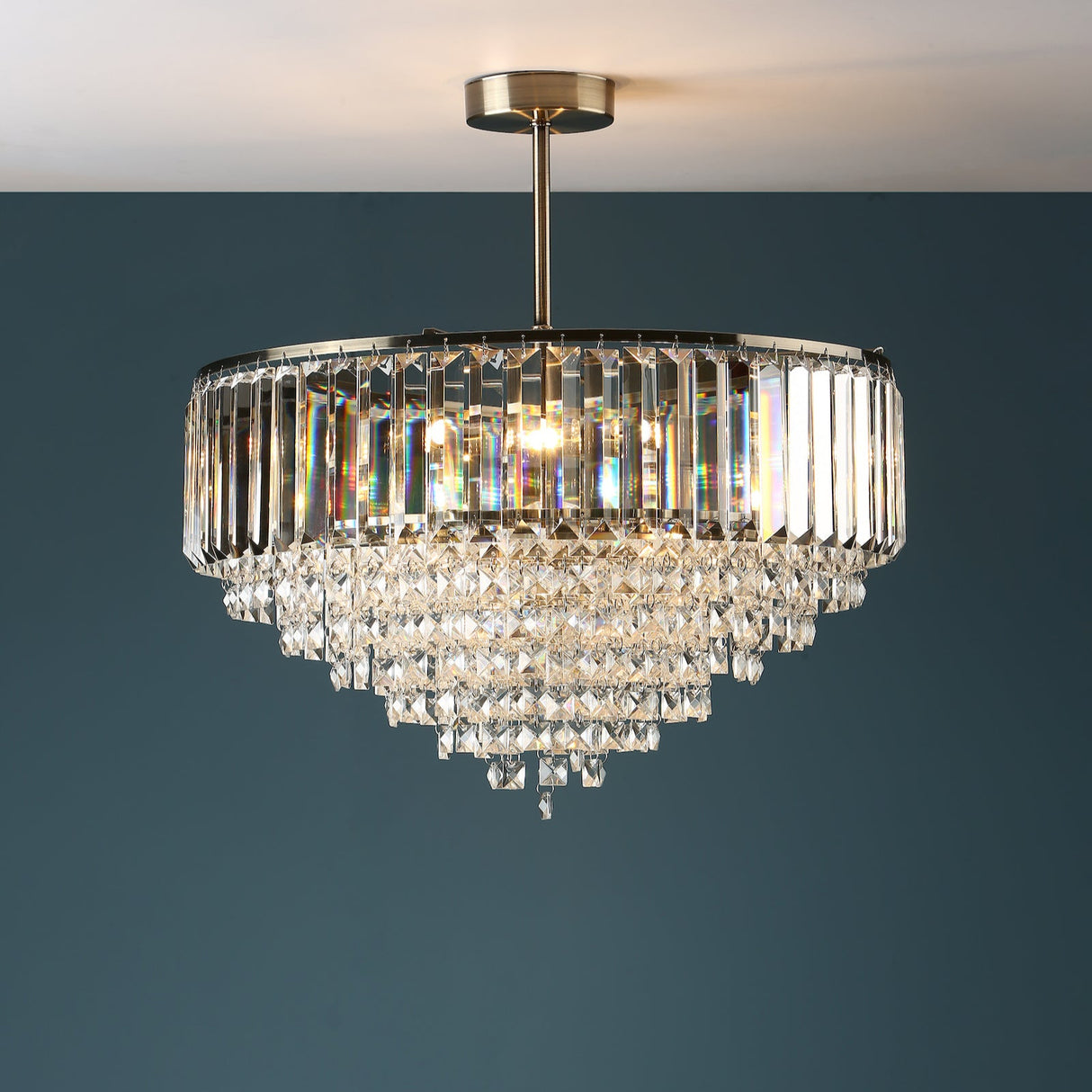 Modern crystal chandelier with tiered prisms and brass fixture against blue wall