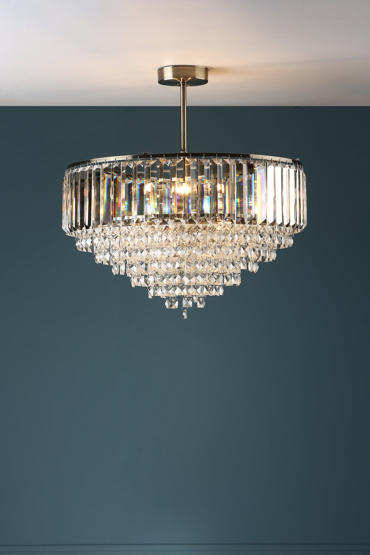 Elegant crystal chandelier with gold metal frame hanging from ceiling against blue wall
