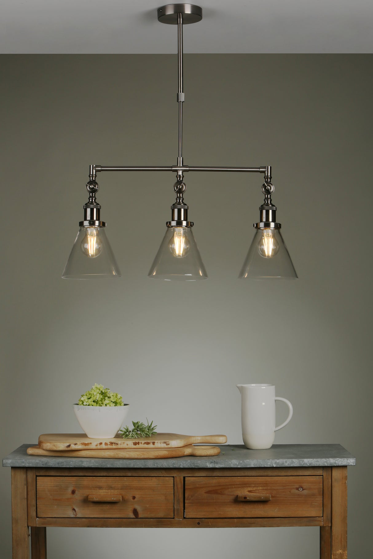 Modern industrial triple pendant light with clear glass shades over rustic wooden table with white bowl and pitcher