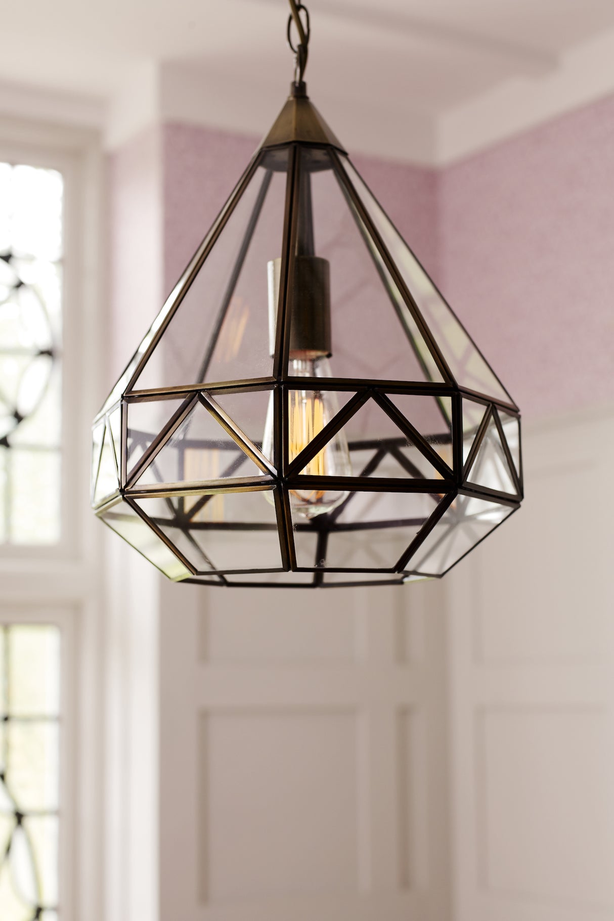 Geometric glass and metal pendant light with Edison bulb hanging in a room with white panel walls