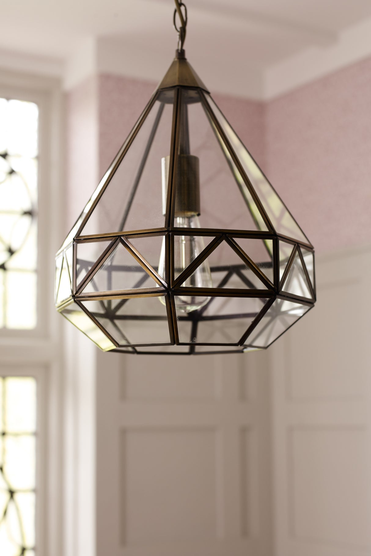 Geometric glass and metal pendant light fixture hanging in a softly lit room with pink wallpaper and white paneled walls