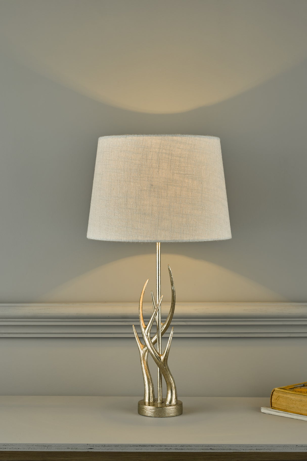 Decorative table lamp with beige fabric shade and metallic antler base on grey surface