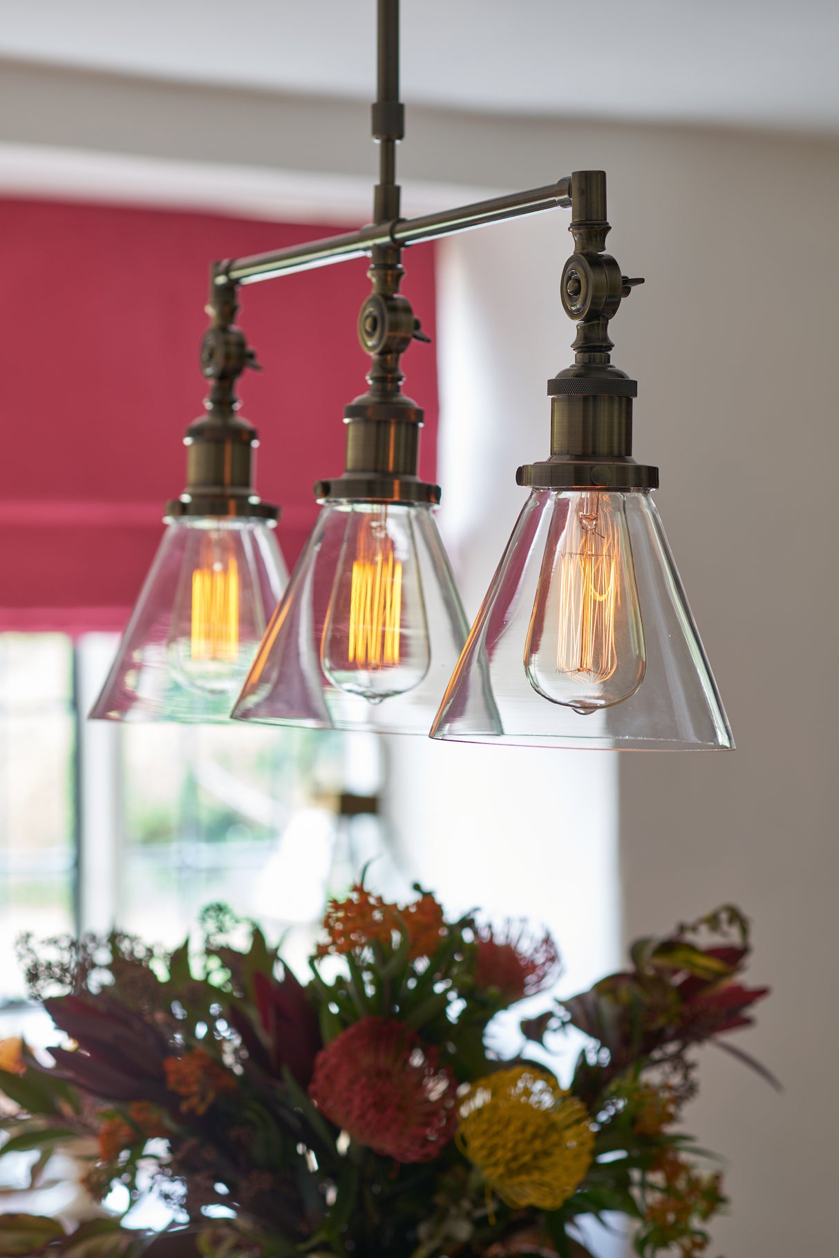 Three vintage-style Edison bulb pendant lights with clear glass shades above colorful floral arrangement