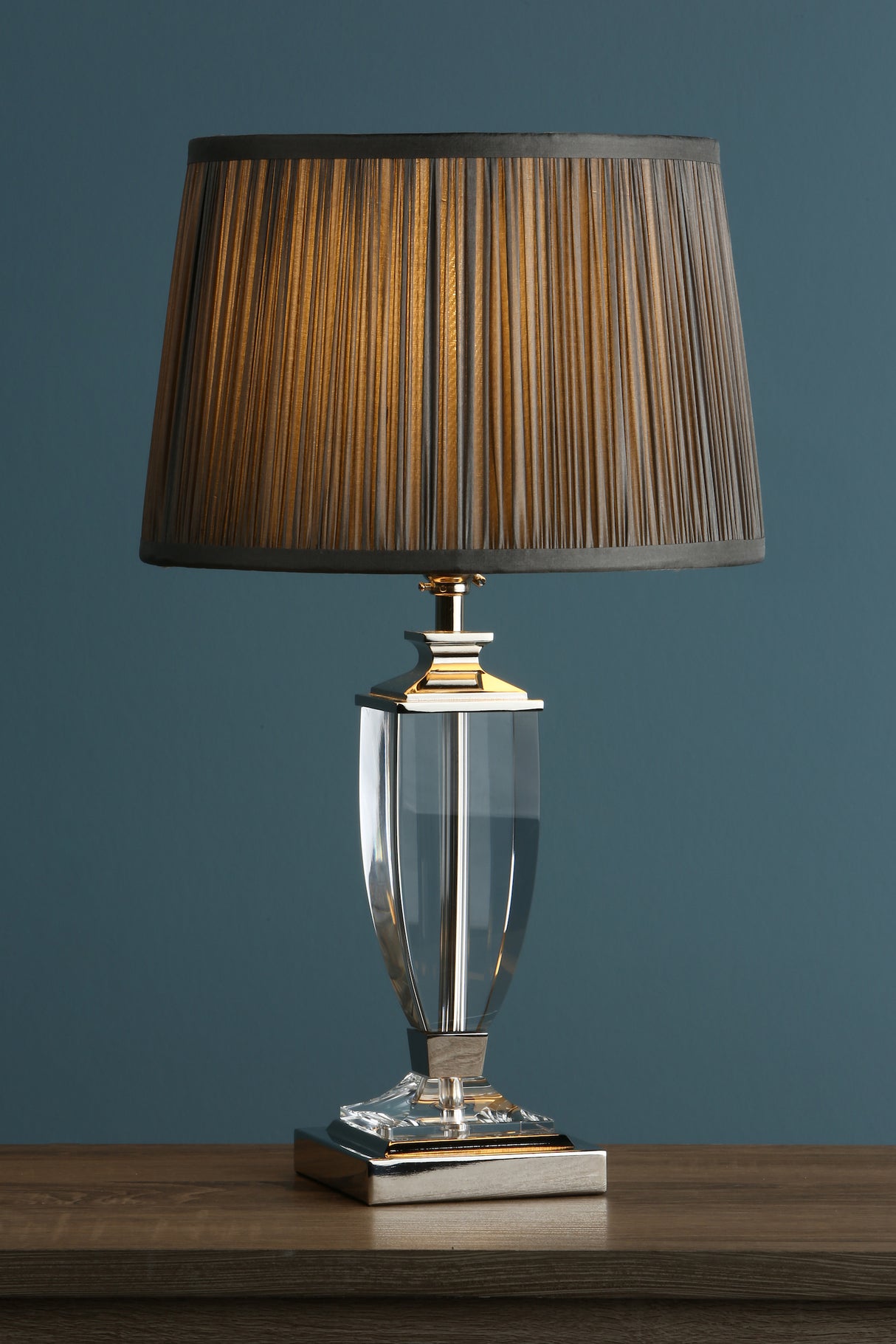 Elegant table lamp with crystal base and pleated gray fabric shade on wooden surface