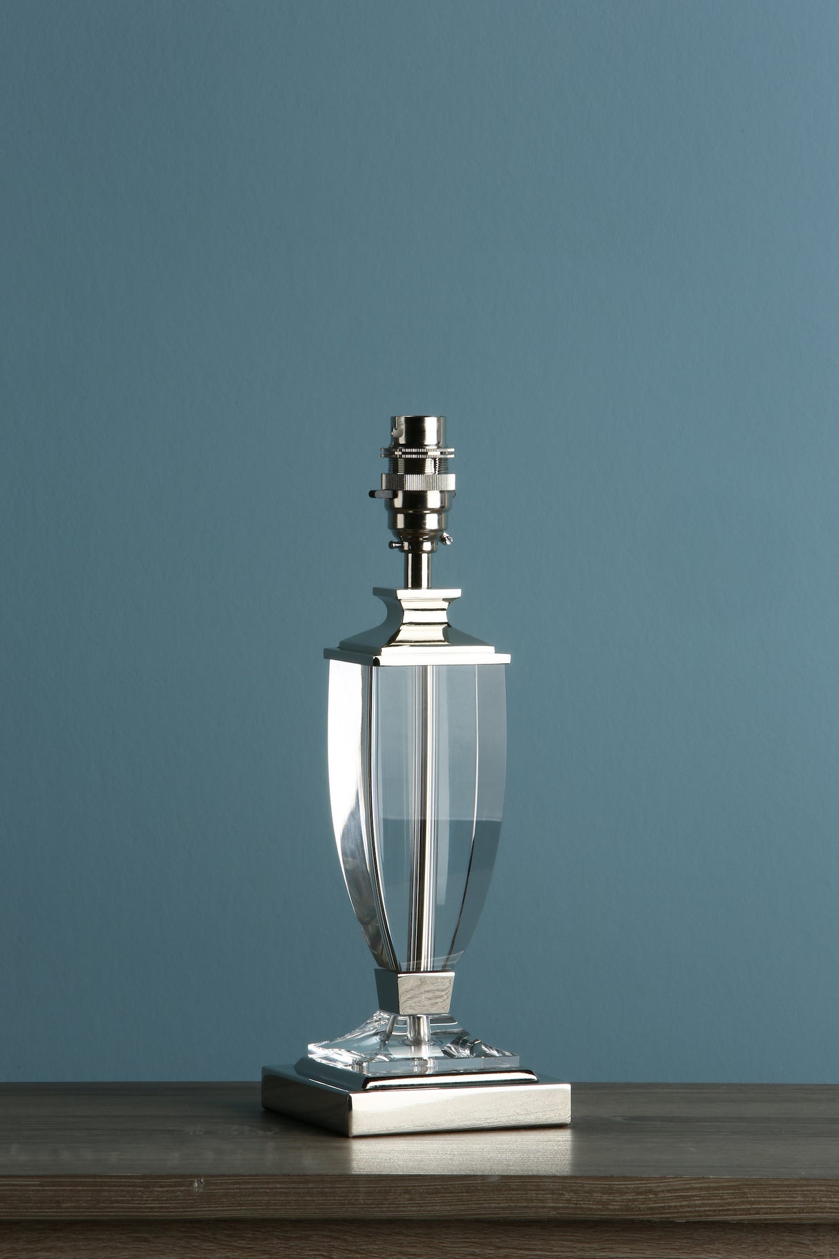 Transparent crystal and polished silver table lamp base on wooden surface with blue wall background